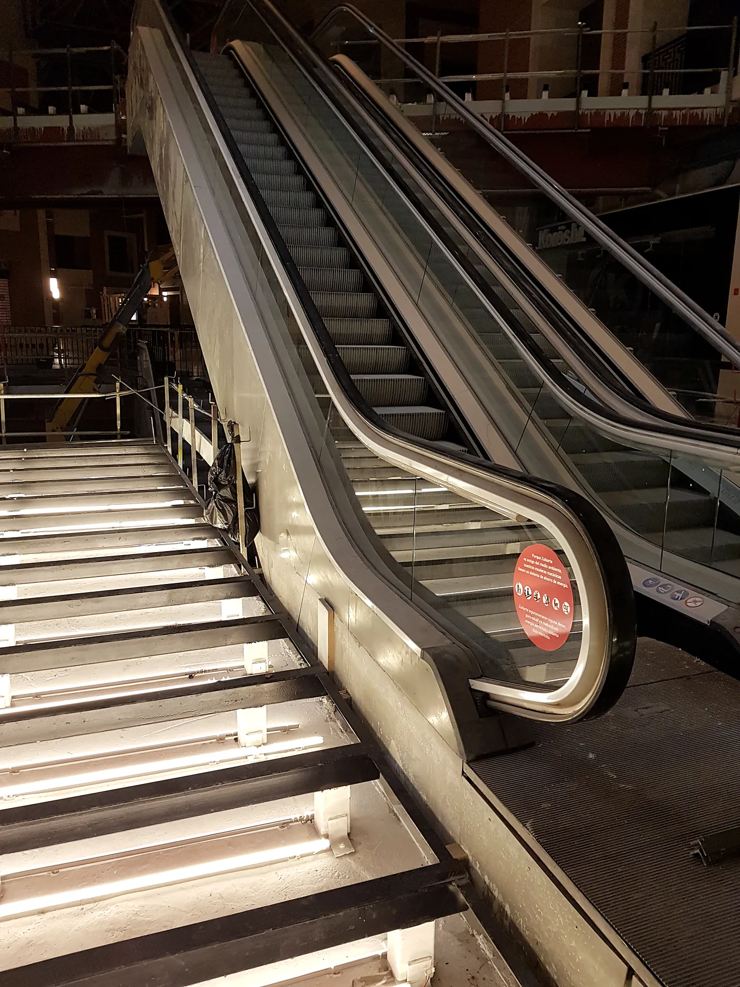 Escalera de vidrio iluminada junto a las escaleras mecánicas